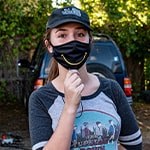 Paola Beck Gisler stands wearing a black mask with a yellow smile.