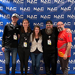 Armada graduates Nathan Duke and Megan Danaher and Full Sail esports staffers Sari Kitelyn, Bennett Newsome, and Jacob Kaplan stand in front of a NACE backdrop.