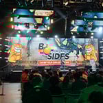 A large audience sits in chairs in front of a stage, which has a digital backdrop that says 2024 B-Side Orlando Chomp Your Own Adventure with two cartoon alligators.