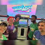 Caris Baker stands with four students in front of an arcade game machine that says Throwback! Jai-Alai Heroes on the screen.