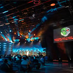 Attendees sit in the Full Sail Live venue. Screens with a lizard robot logo and the words BSides Orlando 2023: Rise of the Robots are on either side of the stage.