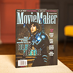 A copy of MovieMaker Magazine sits on a table. An actor in a Blue Beetle costume is on the cover. The headline “The 25 Best Film Schools & Coolest Film Festivals” runs across the top.