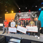 Techfest tournament winners holding large scholarship checks on stage alongside Full Sail staff members in the Fortress.