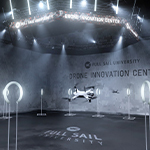 A white drone flies in the netted airspace in Full Sail’s Done Innovation Center. It is surrounded by white rings on stands.