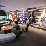 An image of Full Sail’s Military Student Success center shows a large couch, small meeting rooms, and flags representing each branch of the US Armed Services.