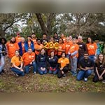 A group photo of students and staff wearing bright orange Full Sail University t-shirts. They are also holding golden balloons that spell 200.