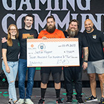 Sam Lupo, DrLupo, Bennett Newsome, and Kevin Murray on stage in the Fortress with a student in an orange Armada jersey receiving an oversized scholarship check.