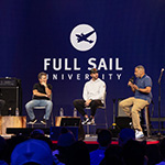 MLB Pitcher Adam Wainwright and three other people are seated on a stage during a panel, the large-scale LED screen behind them reads “Full Sail University” against a blue backdrop.