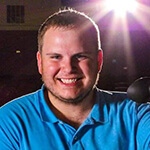 Grad Cody Grammer in a blue collared shirt, holding a video camera in a movie theater.