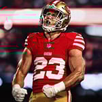 A football player in a red San Francisco 49ers jersey, number 23, celebrating passionately on the field with clenched fists.