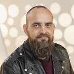 Full Sail Hall of Fame inductee Ben Rice smiles at the camera. He is wearing a burgundy sweater and a black leather jacket.