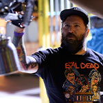 Steven C. Miller adjusts a piece of machinery on a science lab set. He is wearing an Evil Dead t-shirt.