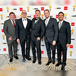 Culley Bunker stands with four special effects artists from Skulley FX in front of a VES Awards backdrop. They are wearing suits and smiling.