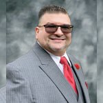 Will Torres wears a gray pinstriped suit with a red tie, a red carnation on the lapel, and sunglasses.