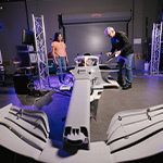 Students and an instructor work with a full-scale race car simulator model inside Full Sail’s Simulation Lab.
