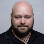 Grad Corey Guerra is wearing a black polo shirt and posing for a headshot against a light grey backdrop.