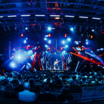 A vibrant charity concert featuring Matt Heafy of Trivium on stage with dynamic lights, a packed audience, and 'Metal + Honey' branding on screen.