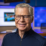 Dan Patrick stands in front of a broadcast desk and smiles at the camera. The words Full Sail University’s Dan Patrick School of Sportscasting are on the right.