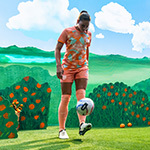 An Orlando Pride player kicks a soccer ball toward a camera on a film set that features an animated orange grove.