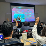 Students sit in an audience facing speakers Sofia Adamary and Gabriella Pedraza. A few students have their hands raised. A projector screen displays “Building With Intention” and a picture of the two speakers.