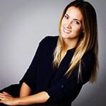 Grad Lisa Maskey, a smiling woman with straight blond hair wearing a black three-quarter sleeve top seated against a grey backdrop.