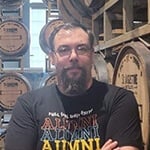 Daniel Vanallen sits in a chair at St. Augustine Distillery Co. He is smiling and wearing a Full Sail Alumni shirt.