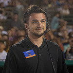 Full Sail grad Joe Zollo wears a headset on the field as Show Coordinator for the Savannah Bananas, with fans filling the stands behind him.