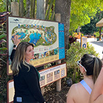 Crystal O’Hea stands at a map of Discovery Cove and speaks to students as they stand around.