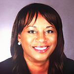 Lorraine smiles at the camera. She has dark brown hair and hazel eyes and is wearing a blue blazer and silver earrings.