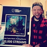 Jordan Moed stands in his studio and holds an award for 10,000 streams for his song “Finding Atlantis.”