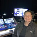 Jean Fuemmeler sits in front of live event video production controllers. She is wearing a gray jacket and smiling.