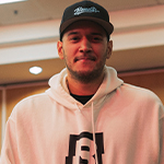 A man standing against a wood paneled wall in a white hooded sweatshirt featuring the Bandits logo and a black Bandits Gaming snapback cap.