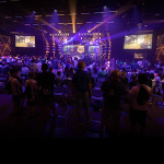 A large crowd in a venue spectating an esports match, a larg LED screen in the front of the room reads ‘North American Finals.’