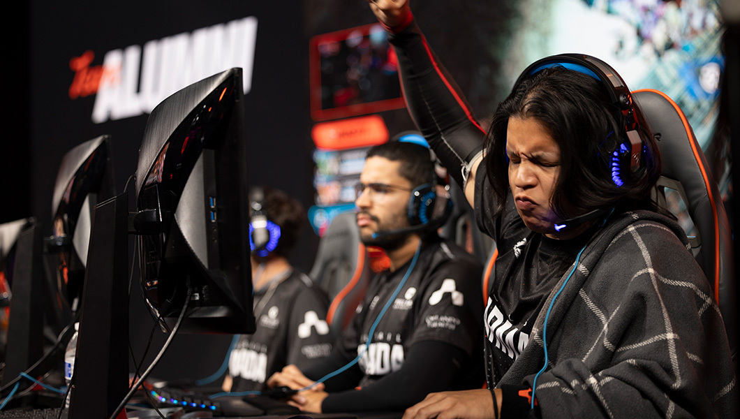 Armada team members sit at consoles and wear headsets as they compete in Hall of Game: Homecoming. One competitor raises their fist in the air in triumph.