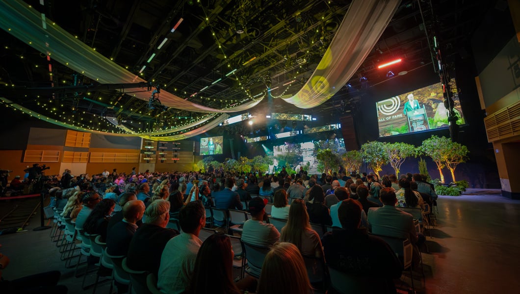 Full Sail President Garry Jones speaks to an audience. Plants, drapes, and lights decorate the stage and ceiling.