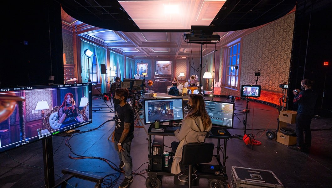 An actor sits in a Victorian-era virtual production backdrop while crew members work on computers.