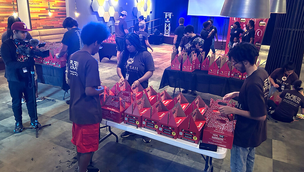 Full Sail volunteers and members of the Agape Roots Foundations assemble care packages atop tables at the Full Sail Treehouse.