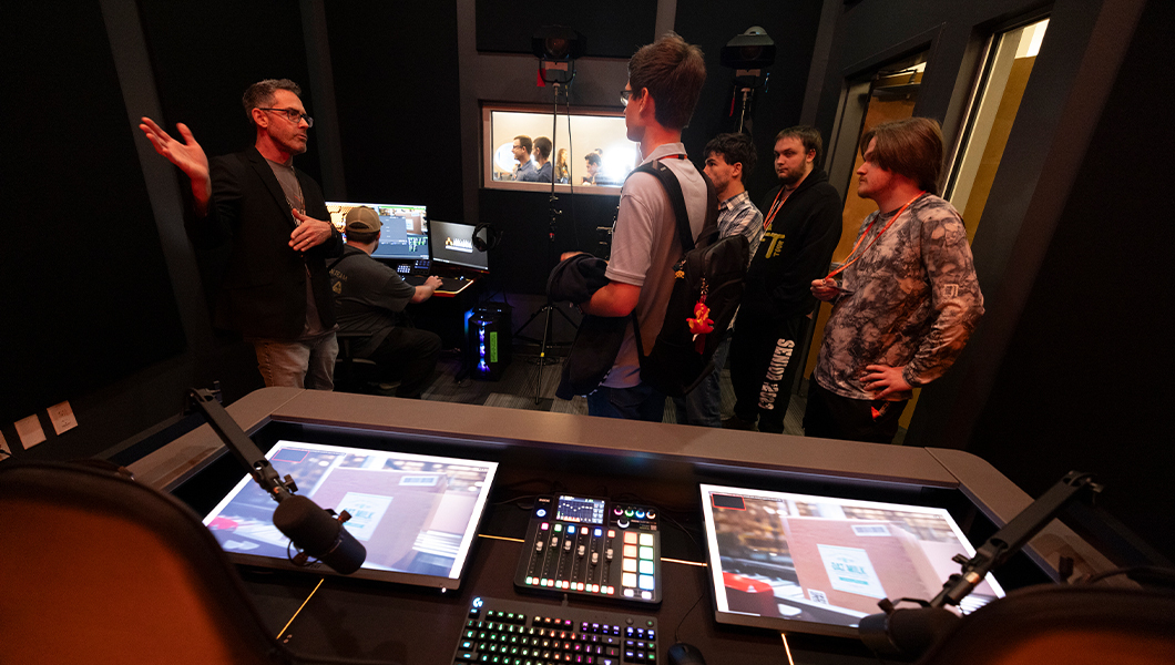 A broadcast studio tour shows streaming equipment, LED panels, and a presenter explaining esports production to students.