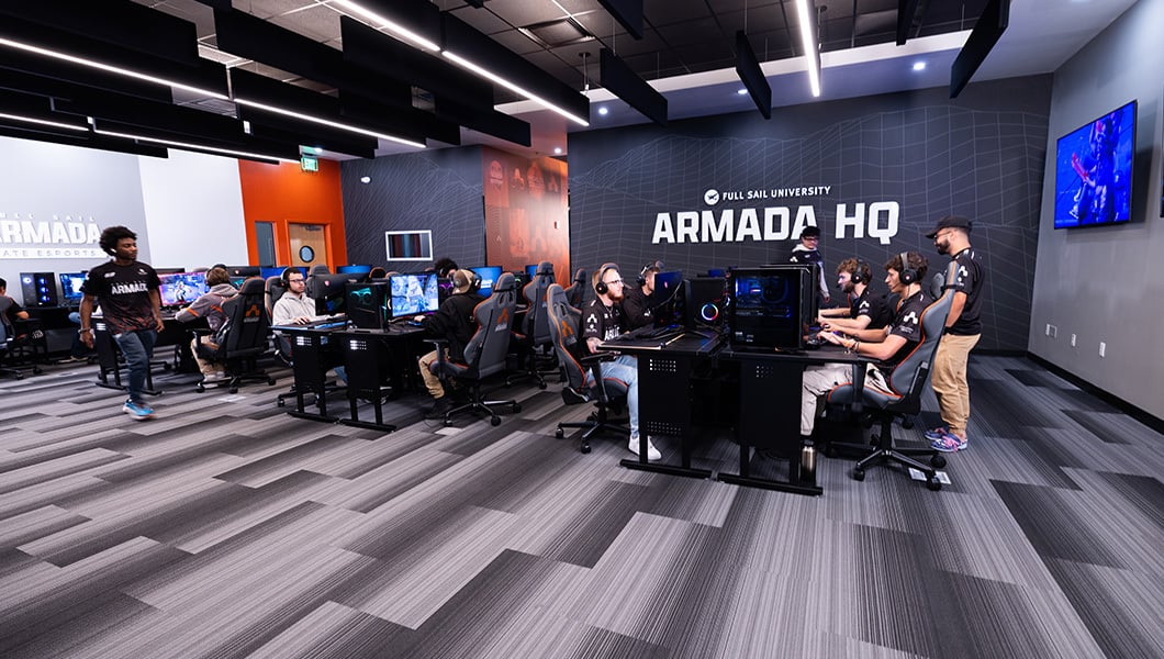 A wide shot of a large room with a sign that reads “Armada HQ” and dozens of students playing at PC gaming stations.