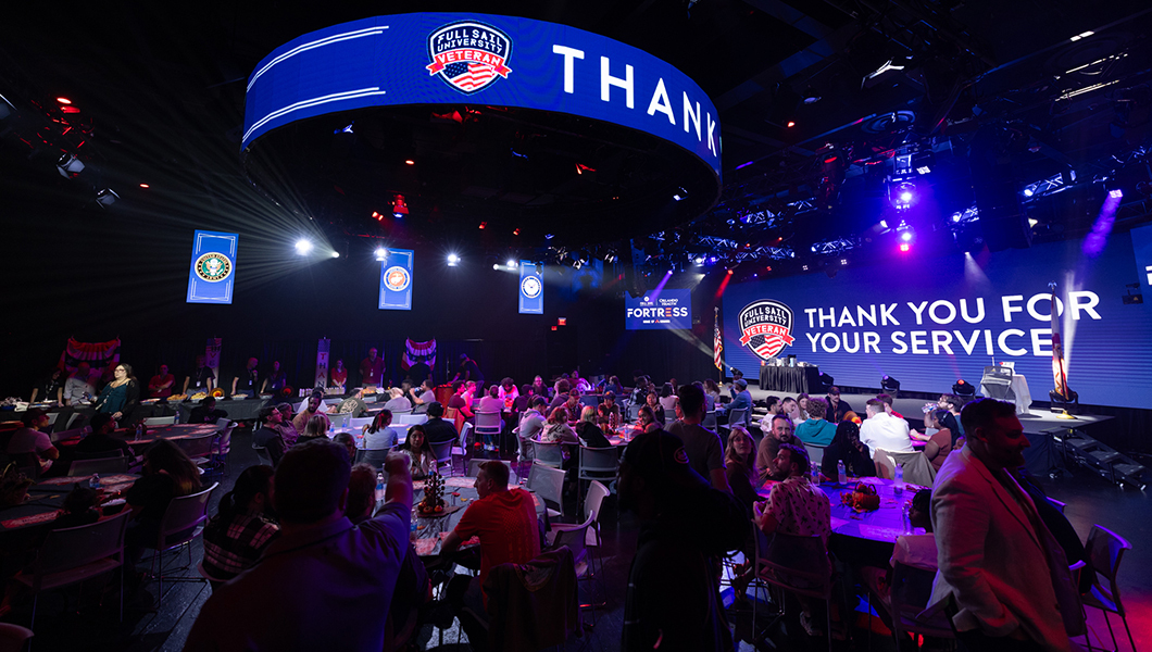 Dinner attendees sit at tables in the Fortress. A screen saying “Thank You For Your Service” is displayed on the venue’s wall.