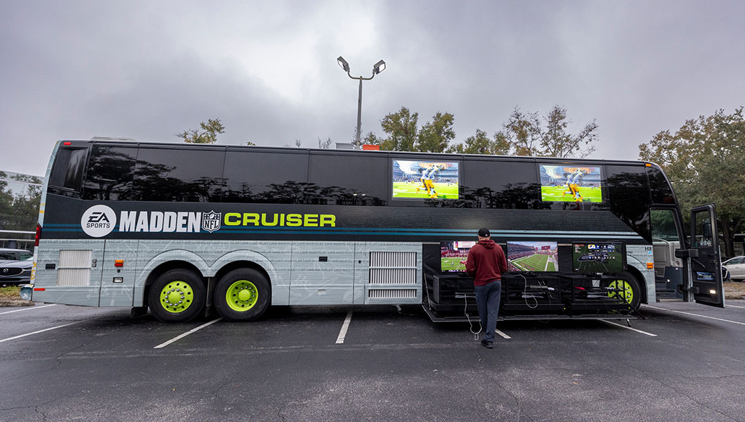 The ‘Madden’ Cruiser, a custom EA Sports gaming bus with outdoor screens displaying Madden NFL, parked in a lot.