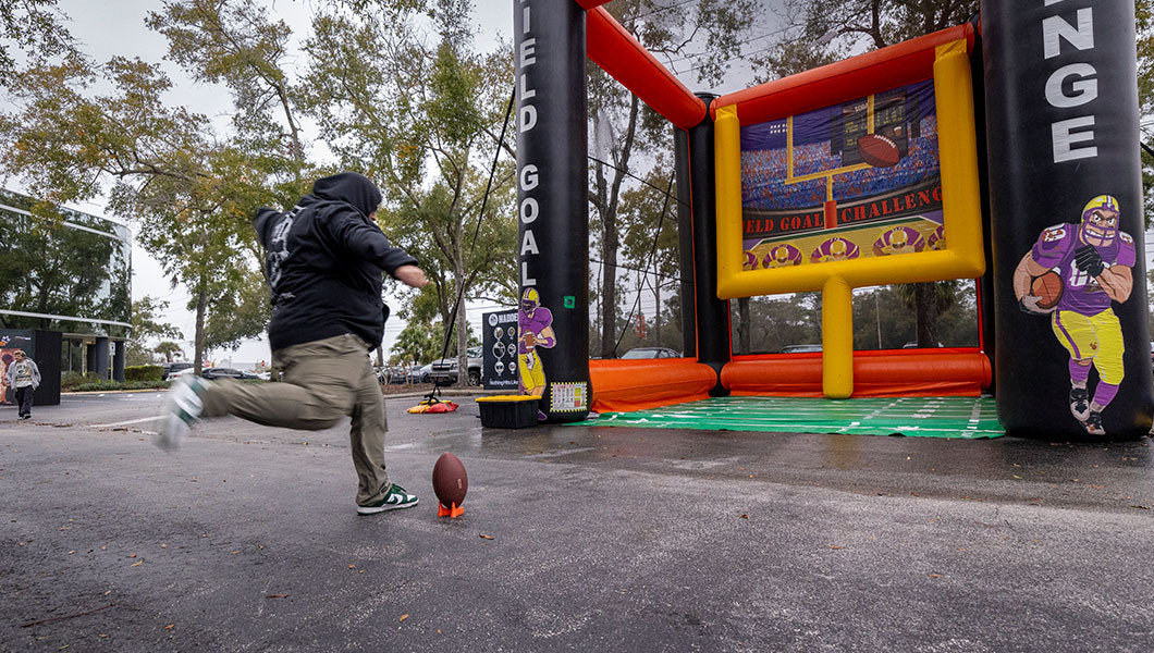 A person kicks a football towards an inflatable field goal game outside of the Full Sail University Orlando Health Fortress.