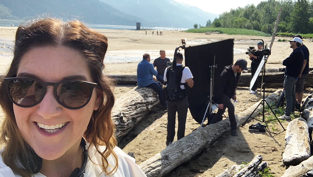 Jenn Miller stands on a beach in Juneau, Alaska. A film crew sets up lighting equipment behind her.