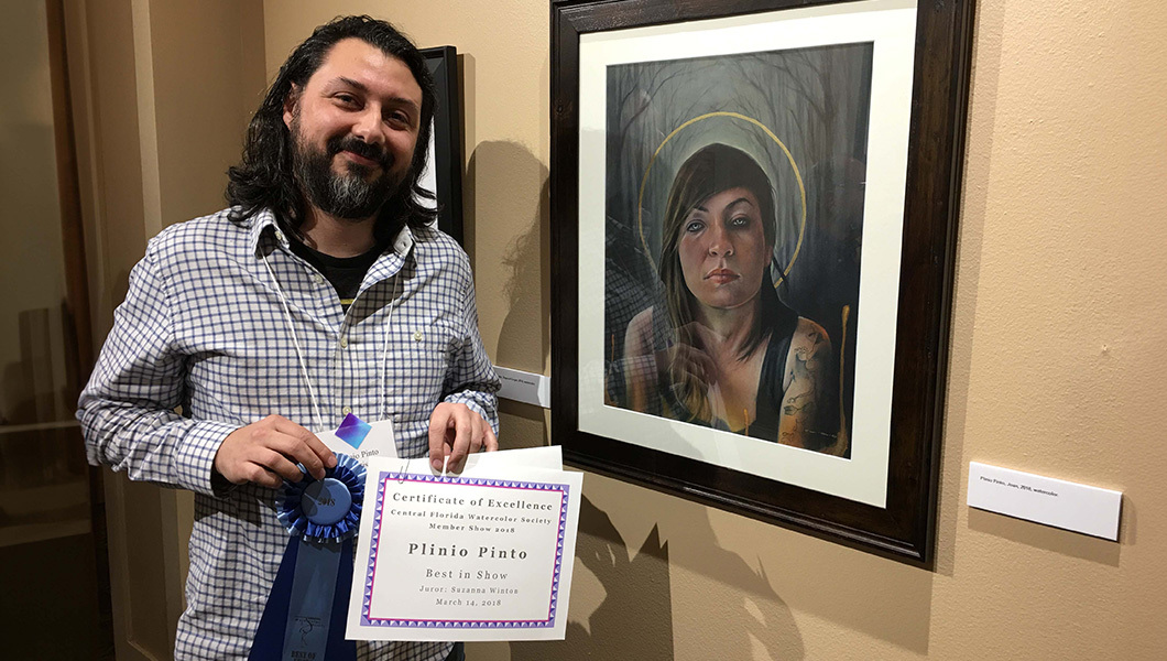 A smiling man stands next to a watercolor portrait of a woman. He is holding a blue ribbon and a Best in Show certificate.