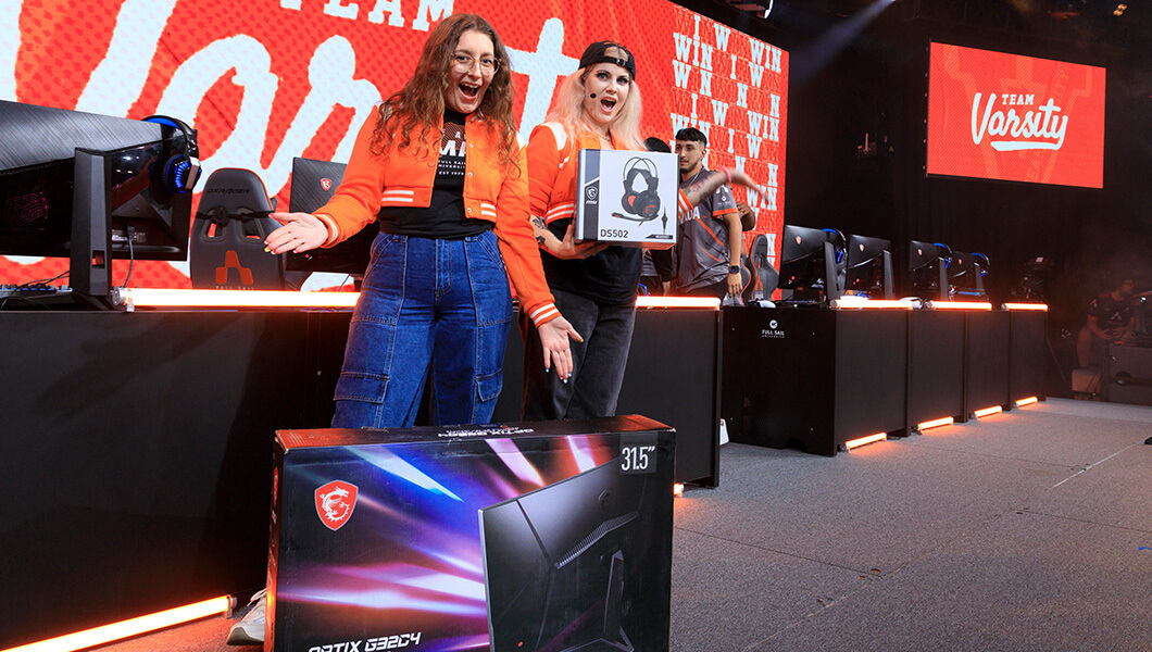 Two people in matching orange varsity jackets on stage while showing off MSI gear.