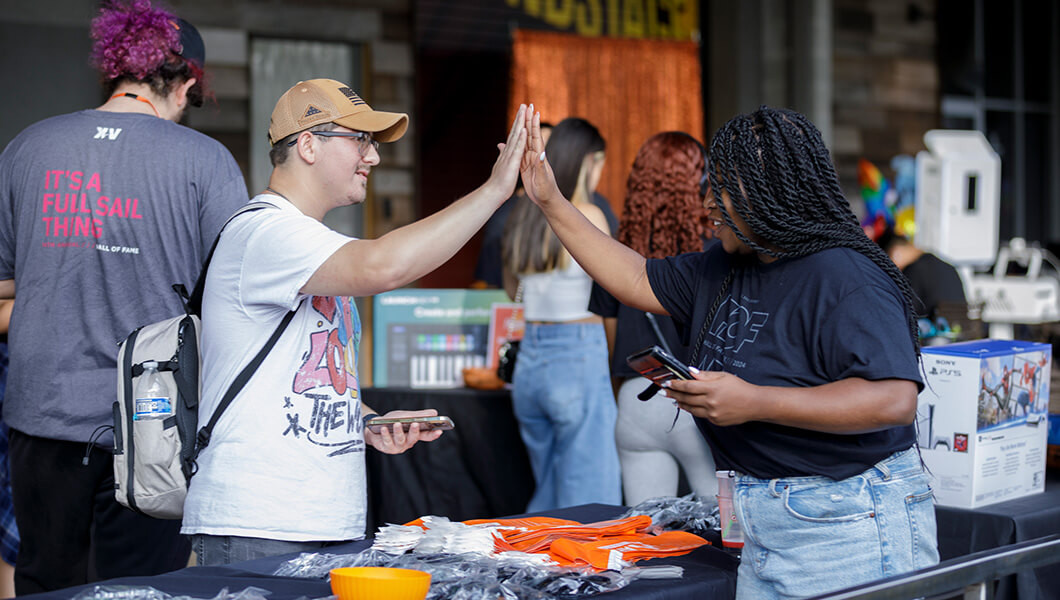 A staff member and student are high-fiving while standing at a table full of Armada merch giveaways.