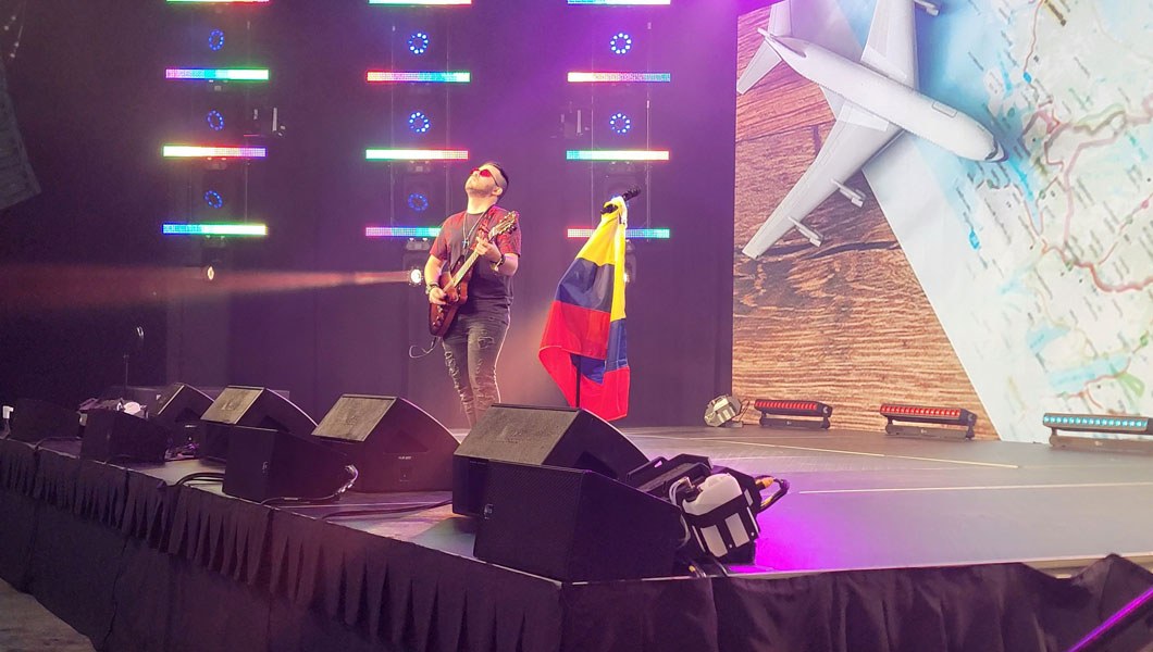 A person is on stage and playing the guitar with the Colombian flag on a flag pole beside them.