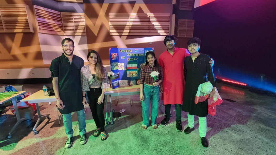 A group of four people standing in front of a table representing India at a cultural festival.