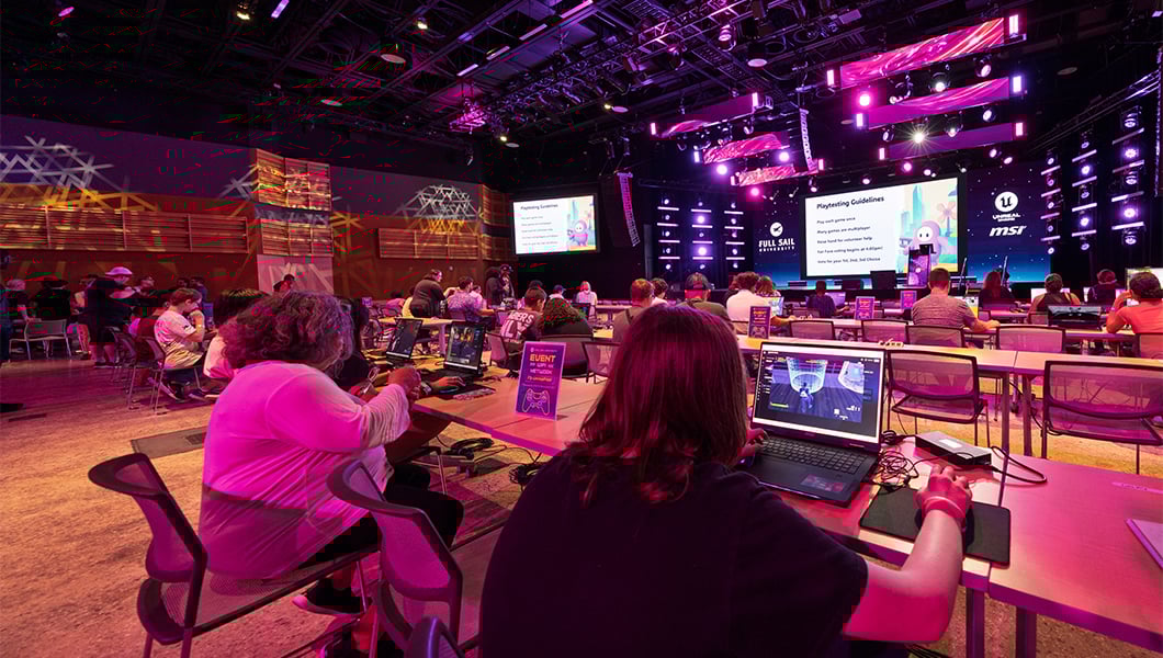 A large venue with rows of workstations featuring gaming laptops and students seated while developing games.