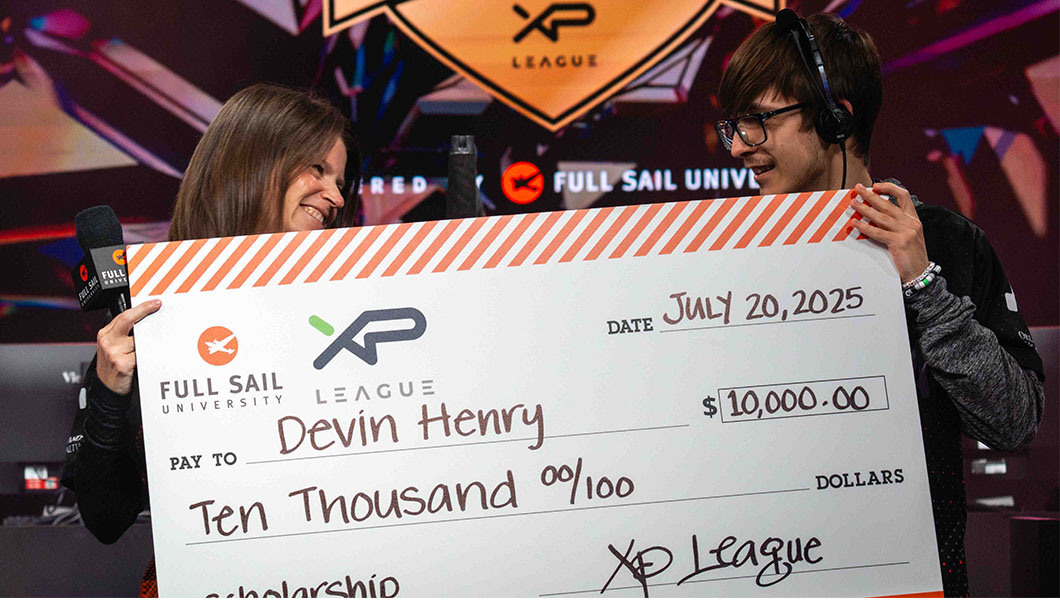 Devin Henry accepts a giant $10,000 check from Sari Kitelyn. Devin wears a headset and glasses and Sari holds a microphone.